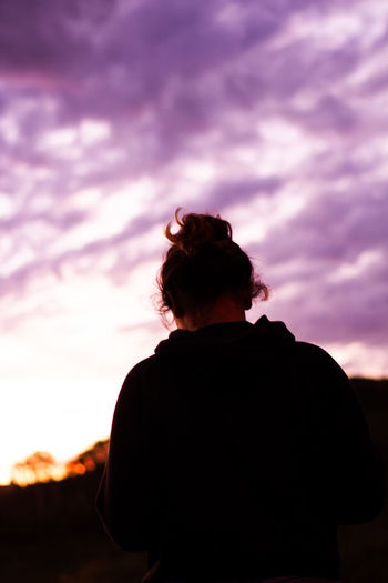 Rear view of girl standing against sky at sunset