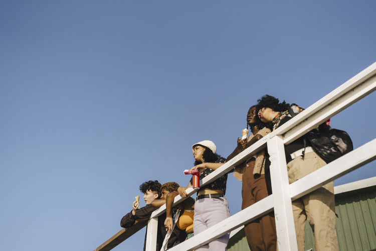Low angle view of multiracial friends hanging out at pier against clear sky