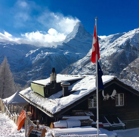 Swiss flag by house against sky during winter