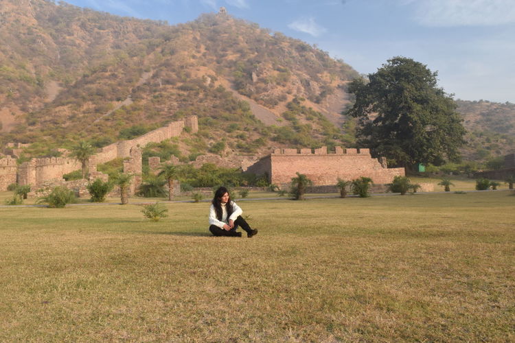 Man sitting on field against mountain