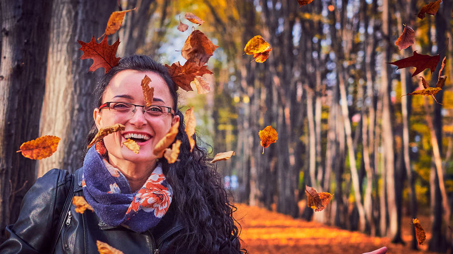 Portrait of smiling young woman with autumn leaves in forest