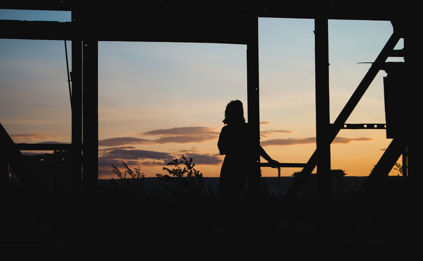 Silhouette people standing by window during sunset