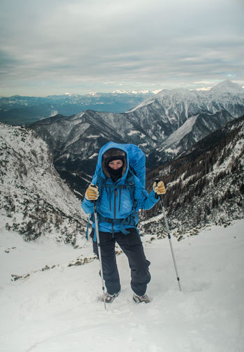 Woman hiking uphill on snowcapped mountain against sky