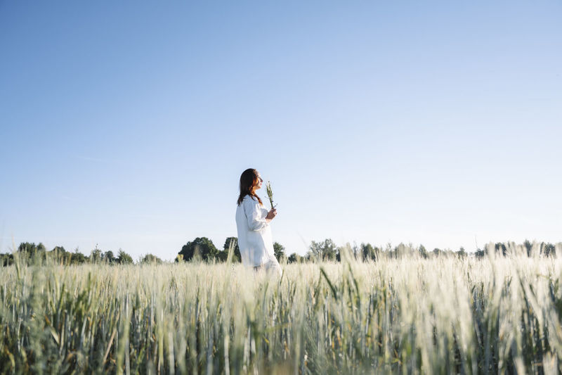Woman walking alone on cornfield under sky