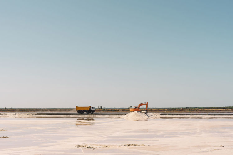 Spain, province of huelva, huelva, clear sky over truck and earth mover working in salt flat