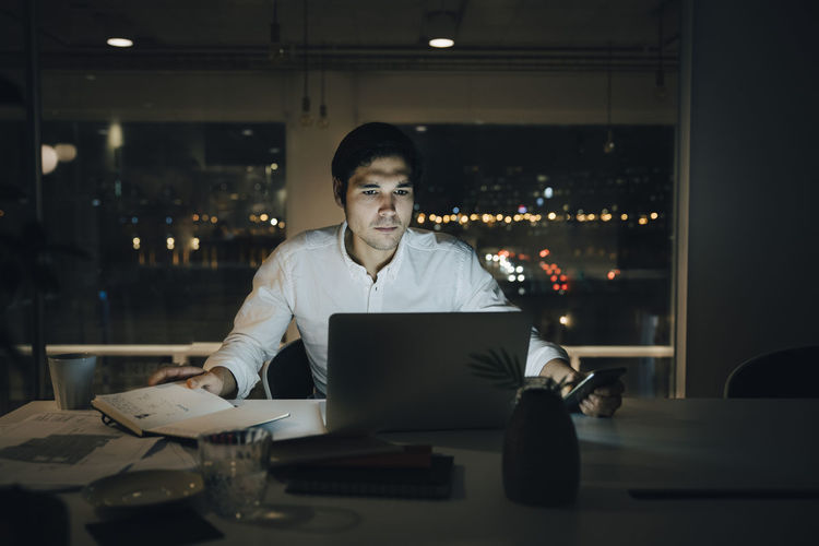 Determined businessman illuminated by laptop while working late in dark office