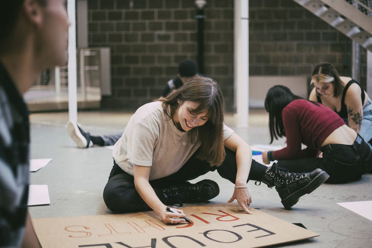 Smiling woman preparing signboard while sitting with male and female activists in building