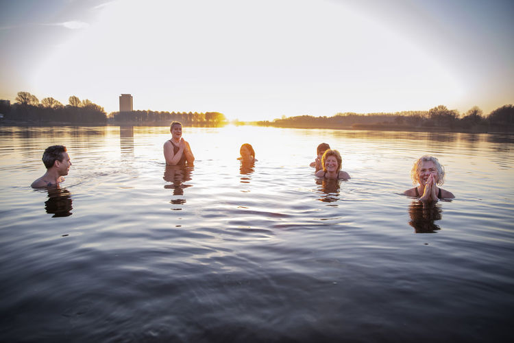 Smiling women meditating while having fun with male friends in water