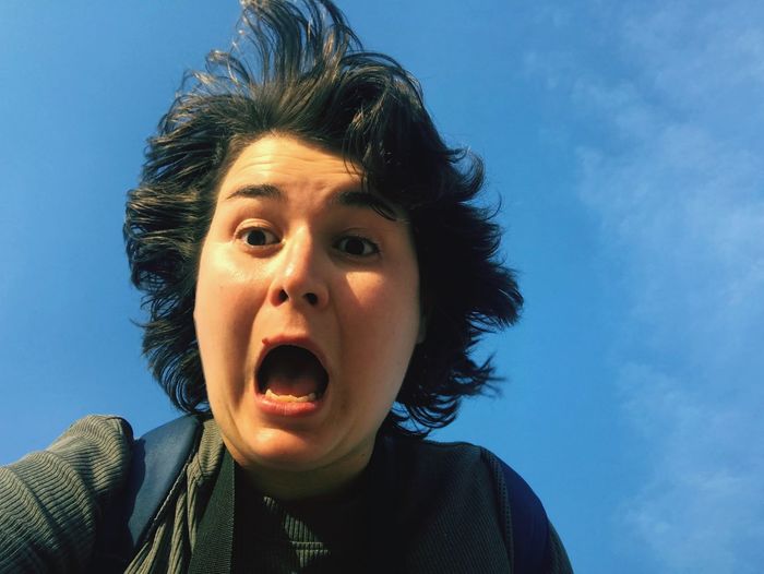 Close-up of woman screaming against blue sky