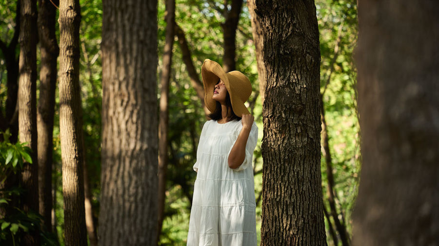 Side view of woman standing by tree trunk in forest