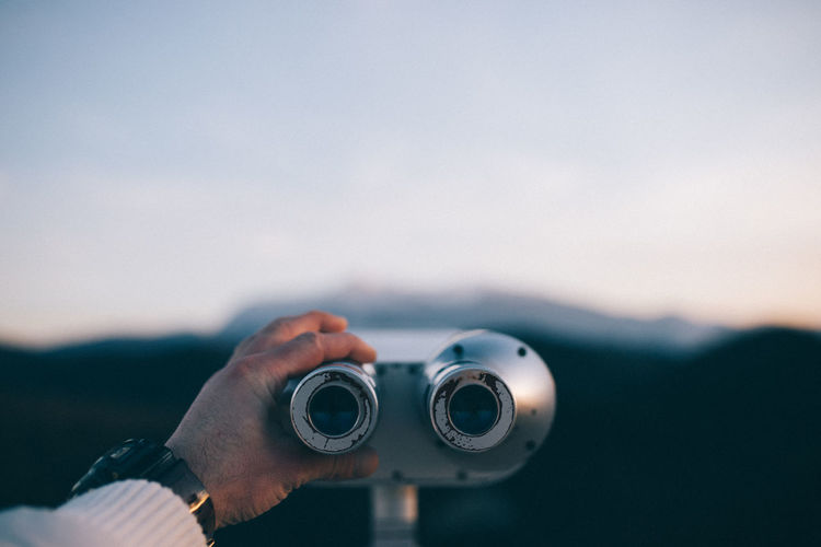 Cropped hand of man holding coin-operated binoculars against sky