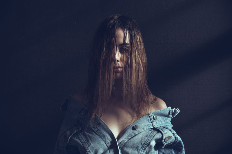 Portrait of sensuous woman wearing denim jacket standing against wall