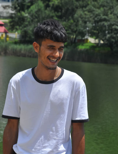 Smiling young man standing against lake