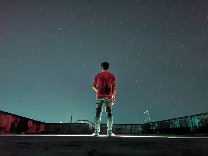 Rear view of man standing against sky at night