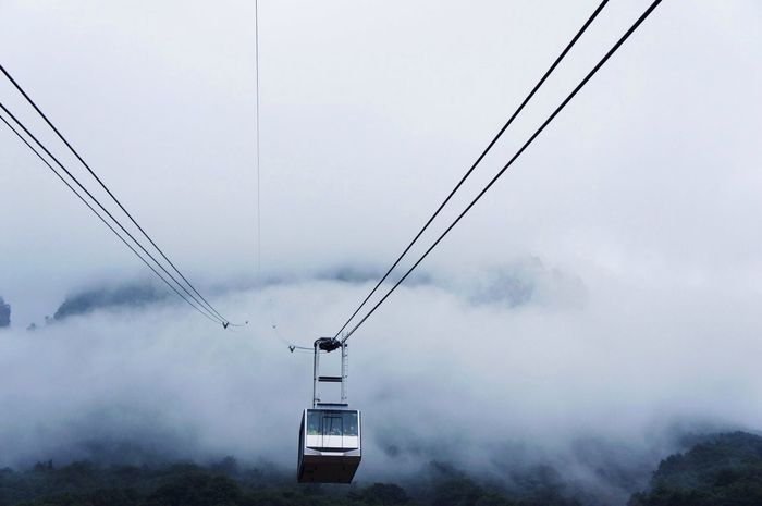 Low angle view of overhead cable car against clouds