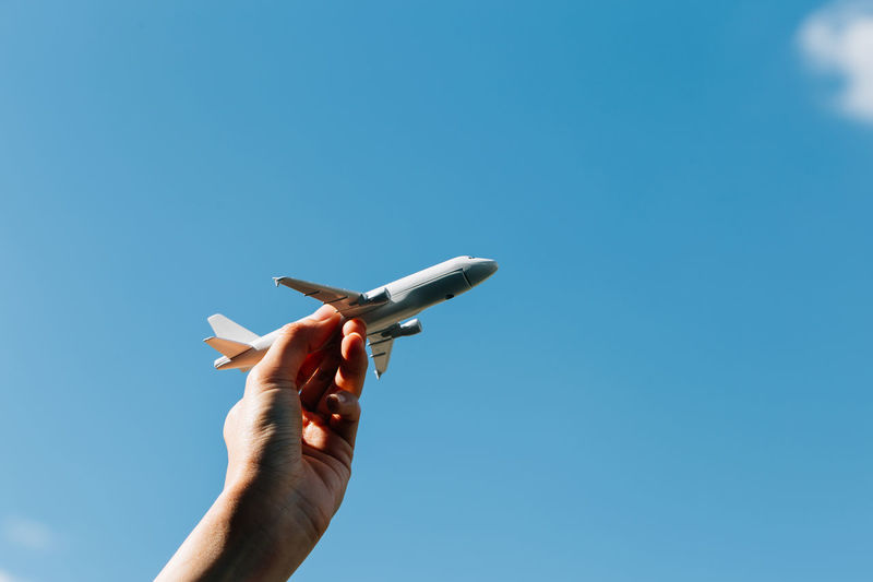 Low angle view of hand holding airplane against clear blue sky
