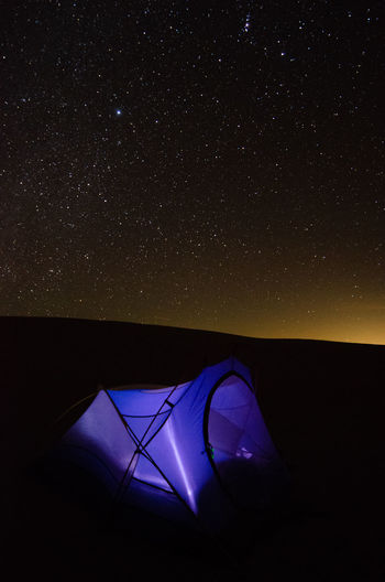 Illuminated tent on mountain against star field at night