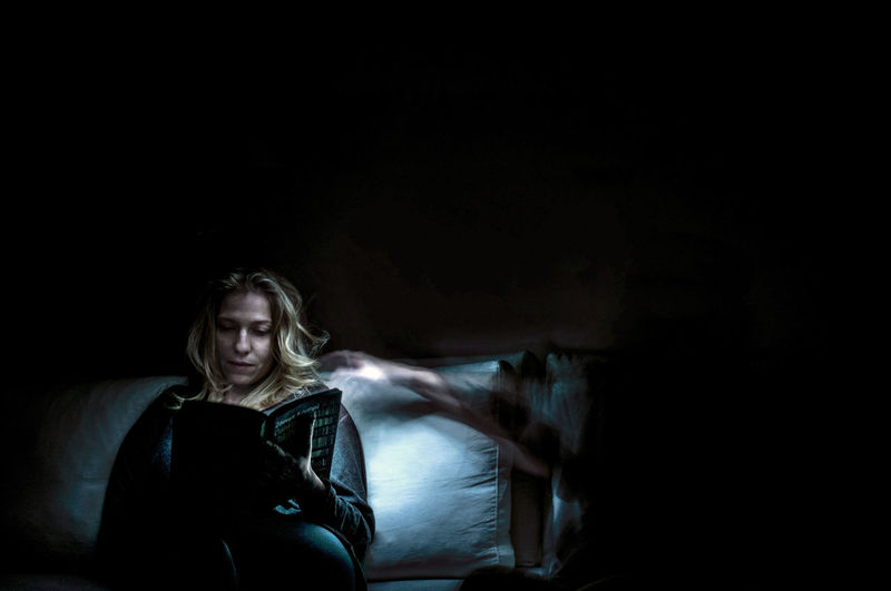 Ghost reaching towards woman reading book in darkroom
