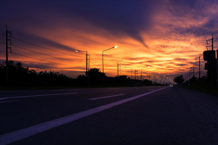 Road by silhouette street against sky during sunset