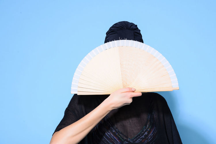 Woman holding hand fan against blue background