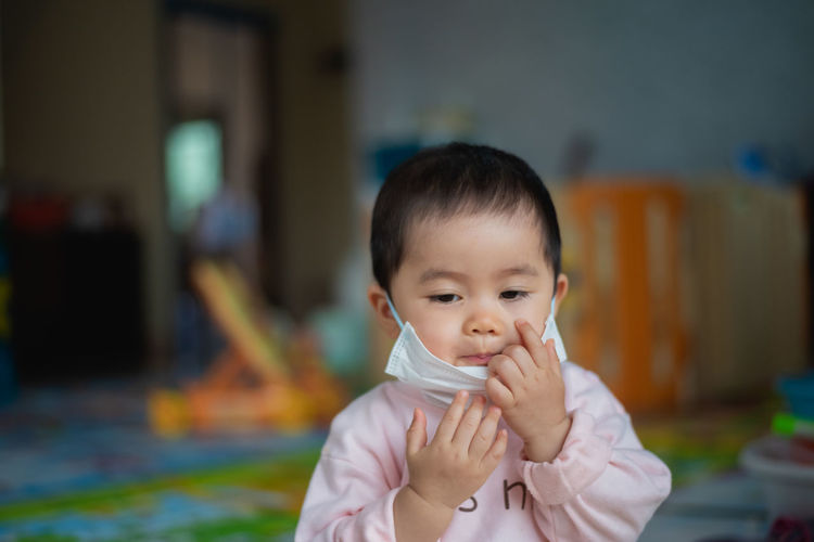 Cute baby girl wearing mask at home