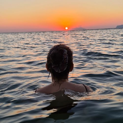 Woman in sea against sky during sunset