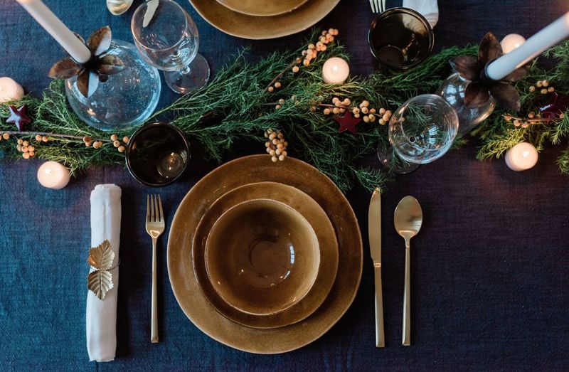 Gold plates & cutlery on a decorated dinner table with greenery