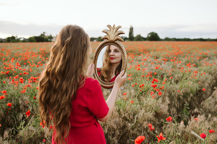 Beautiful young woman by poppy flowers on field against sky