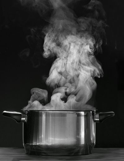 Steaming pot on black background. smoke above boiling soup pot.