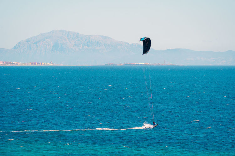 High angle of people doing kite surf on rippling turquoise water of sea with blurred mountains