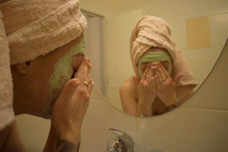 Young woman cleaning facial mask in sink