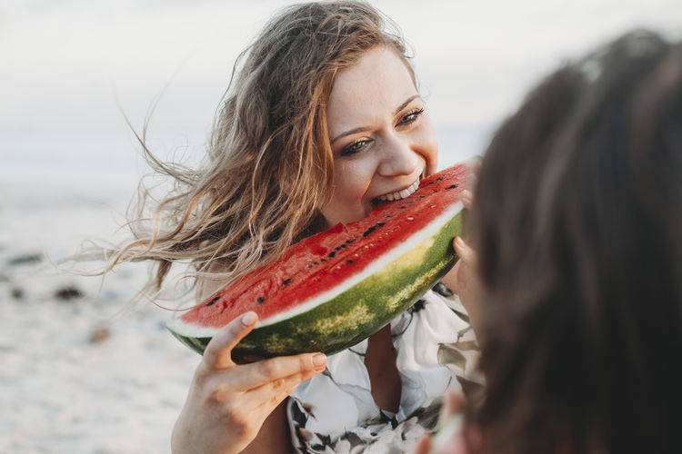 Happy woman eating watermelon with girlfriend at beach