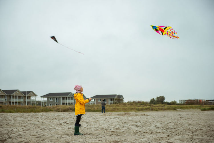 Rear view of boy holding kite standing on beach against sky