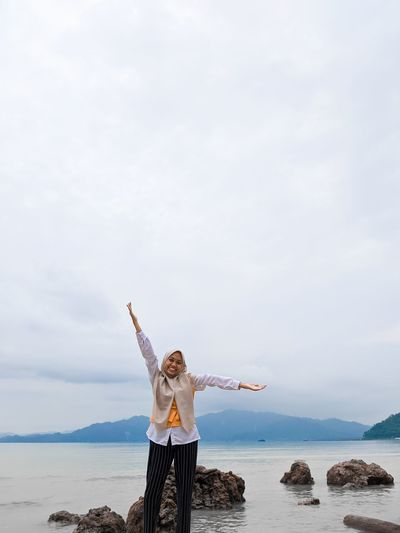 Portrait of woman with arms outstretched standing against sea