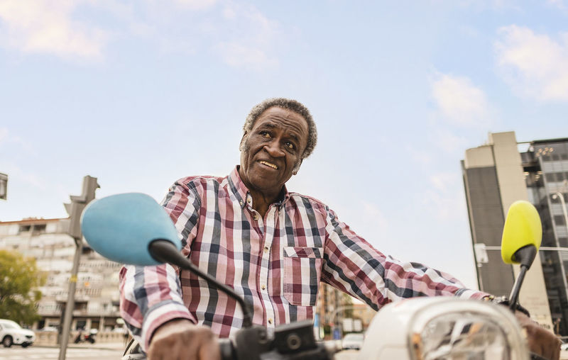 Senior man riding scooter under sky