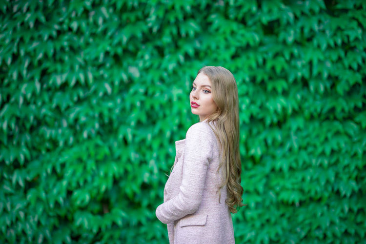 Side view of young woman standing against plants