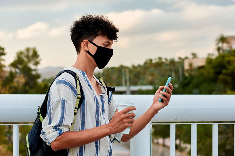 Young afro-haired man with mask is using his mobile on the street