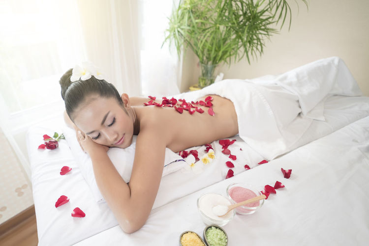 Shirtless young woman with rose petals lying on massage table at spa