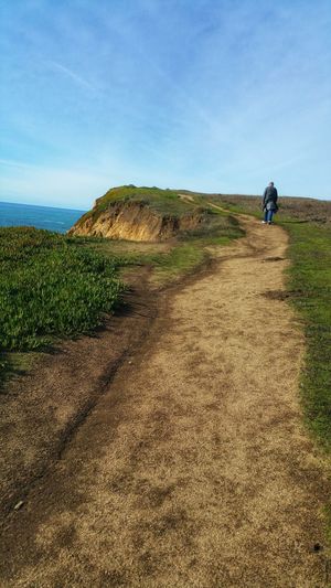Rear view of man on sandstone hiking path at ocean cliff's edge against sky
