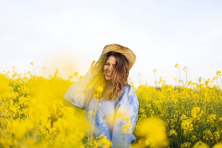 Young woman with yellow flowers on field against sky
