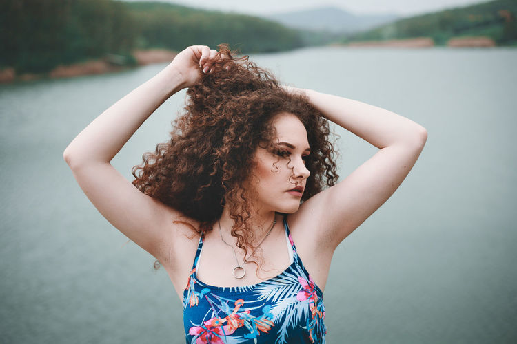 Beautiful young woman with curly hair standing against lake