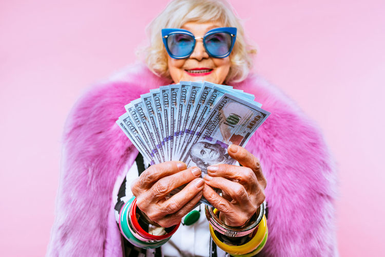 Portrait of senior woman holding banknotes against colored background