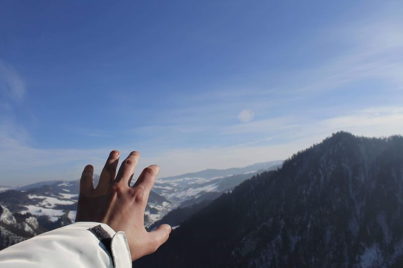 Cropped hand of person gesturing against mountain and sky