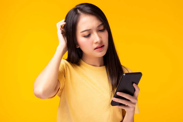 Mid adult man using mobile phone against yellow background