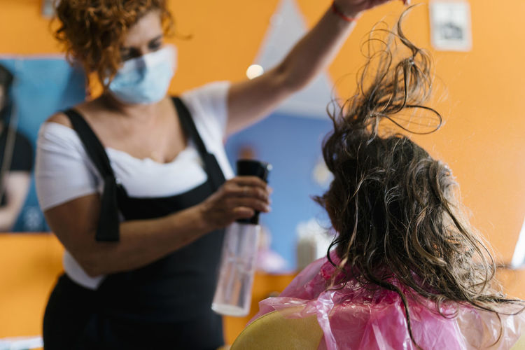 Female hairdresser spraying water on girl's brown hair at barber shop