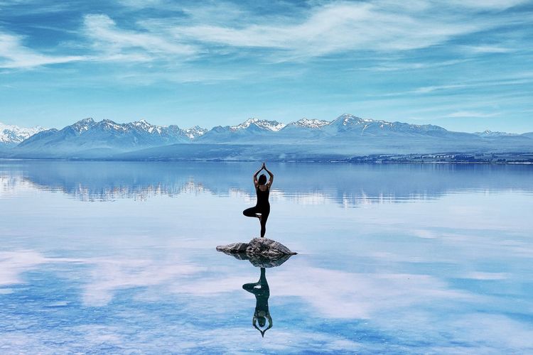 Woman doing yogapose on rock in lake against mountainrange
