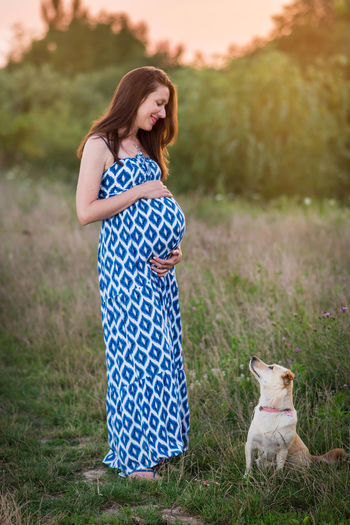 Pregnant woman looking at dog on grassy field