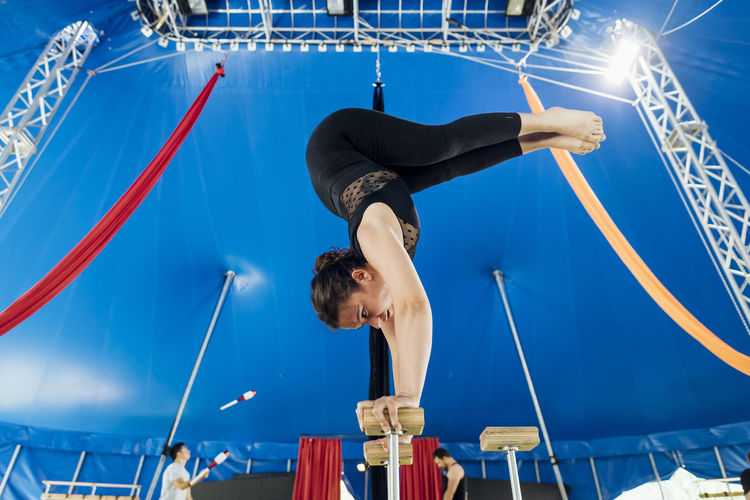 Female acrobat doing rehearsal on handstand cane with athletes in background