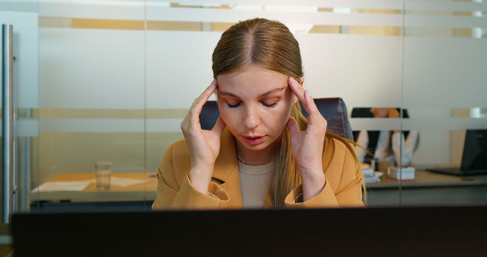 Office worker suffering from migraine in office, massaging temples. 