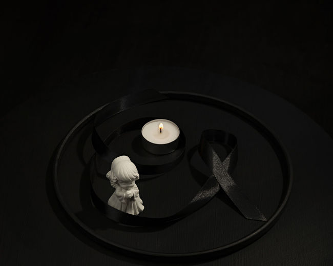 White angel, black mourning ribbon and a candle in dark circle conceptual funeral image